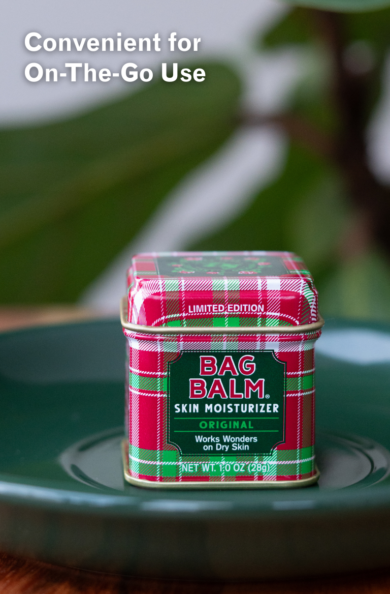 Plaid container of Bag Balm skin moisturizer on a green surface with blurred greenery in the background.