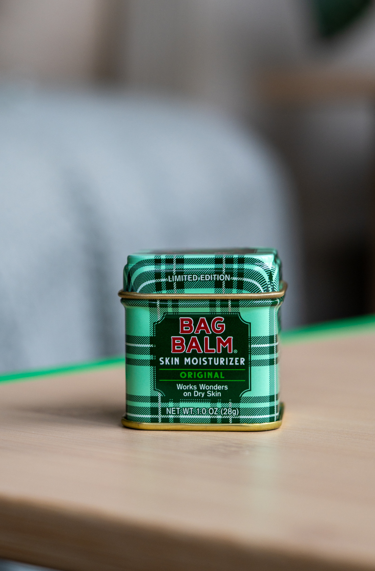 Green tin of Bag Balm skin moisturizer on a wooden surface with a blurred background
