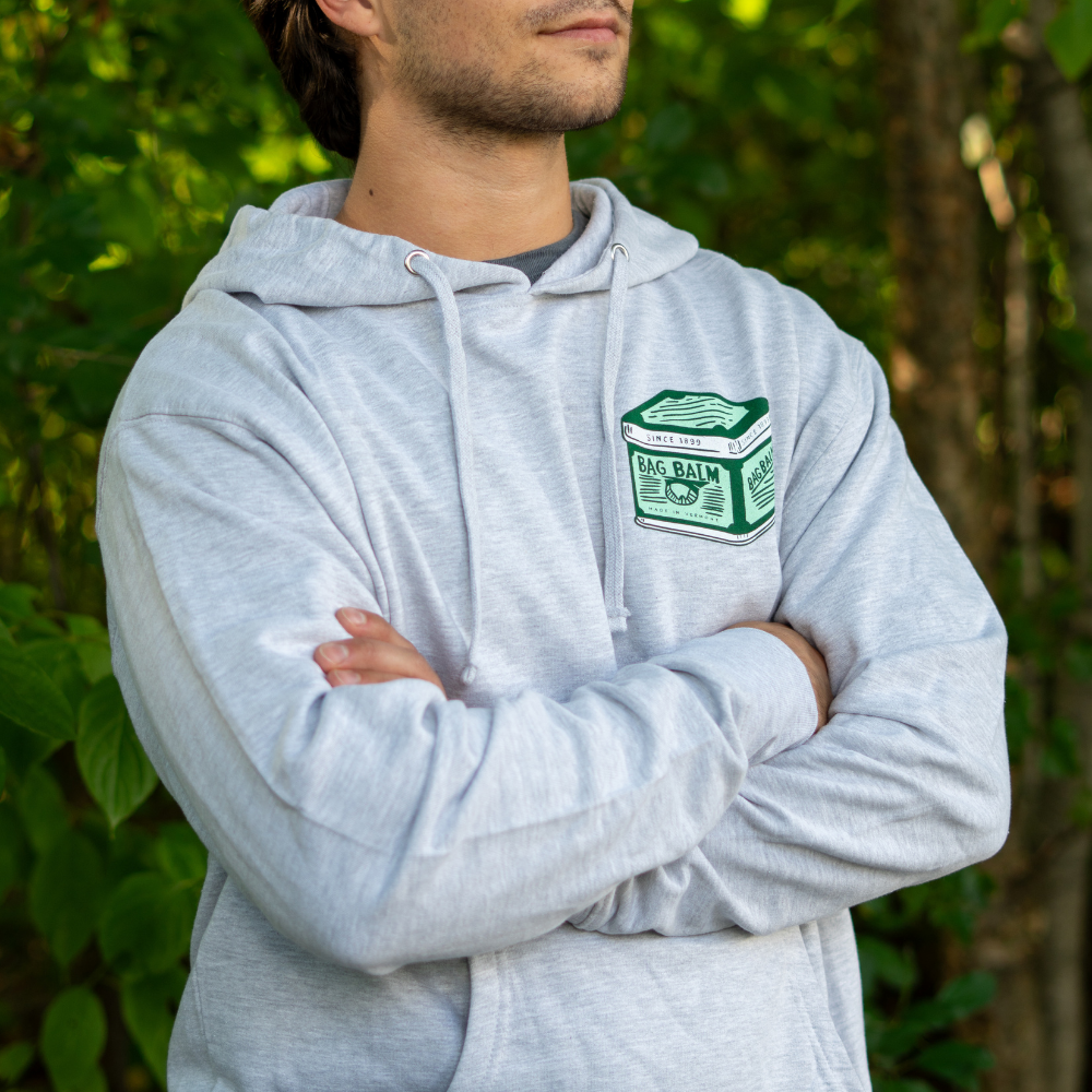Person wearing a gray hoodie with a vintage Bag Balm graphic, standing outdoors.