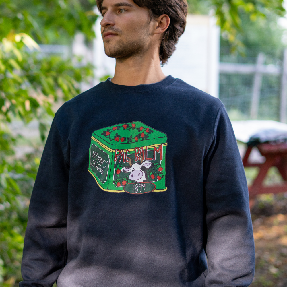 Man wearing a navy blue sweatshirt with a cow + tin graphic design outdoors.