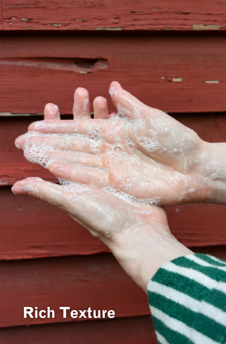 hands with body wash suds on them in front of red wall