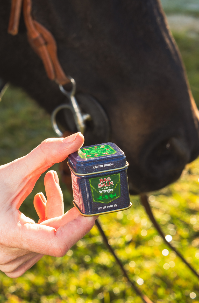 Limited Edition Denim Design Bag Balm 1oz tin in collaboration with Wrangler being held in front of a horse.