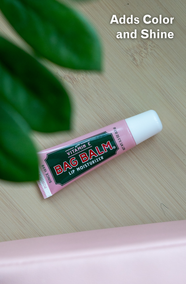 Bag Balm Powder Pink Lip Moisturizer on a wooden surface with leaves in the background.