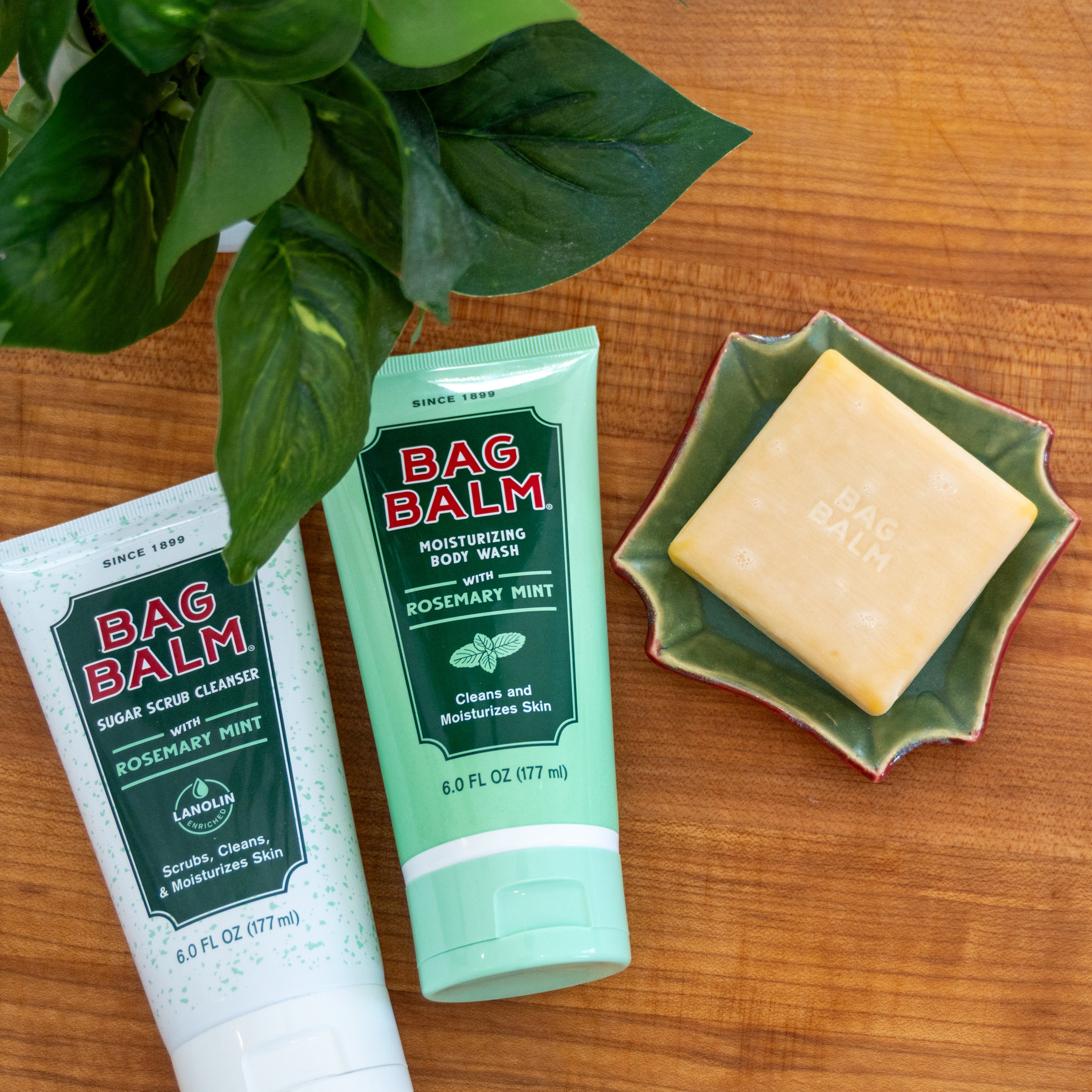 Two bottles of Bag Balm Body Wash and soap next to a bar of soap on a wooden surface.
