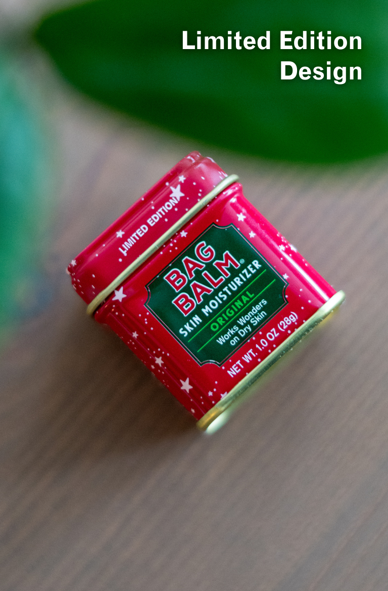 Red with stars container of Bag Balm on a wooden surface with a green leaf in the background.