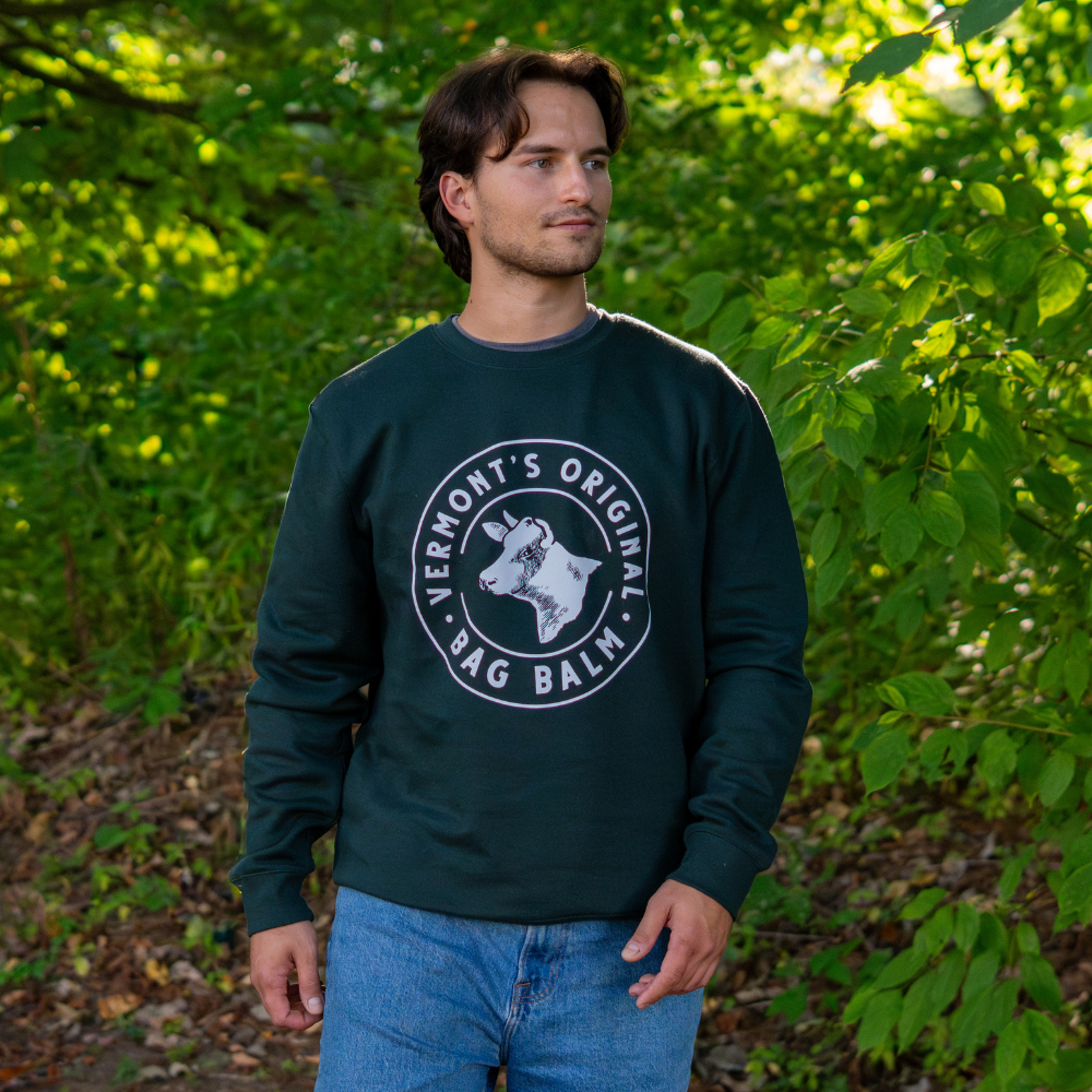 Man wearing a green sweatshirt with a Bag Balm Cow seal logo standing in a forest