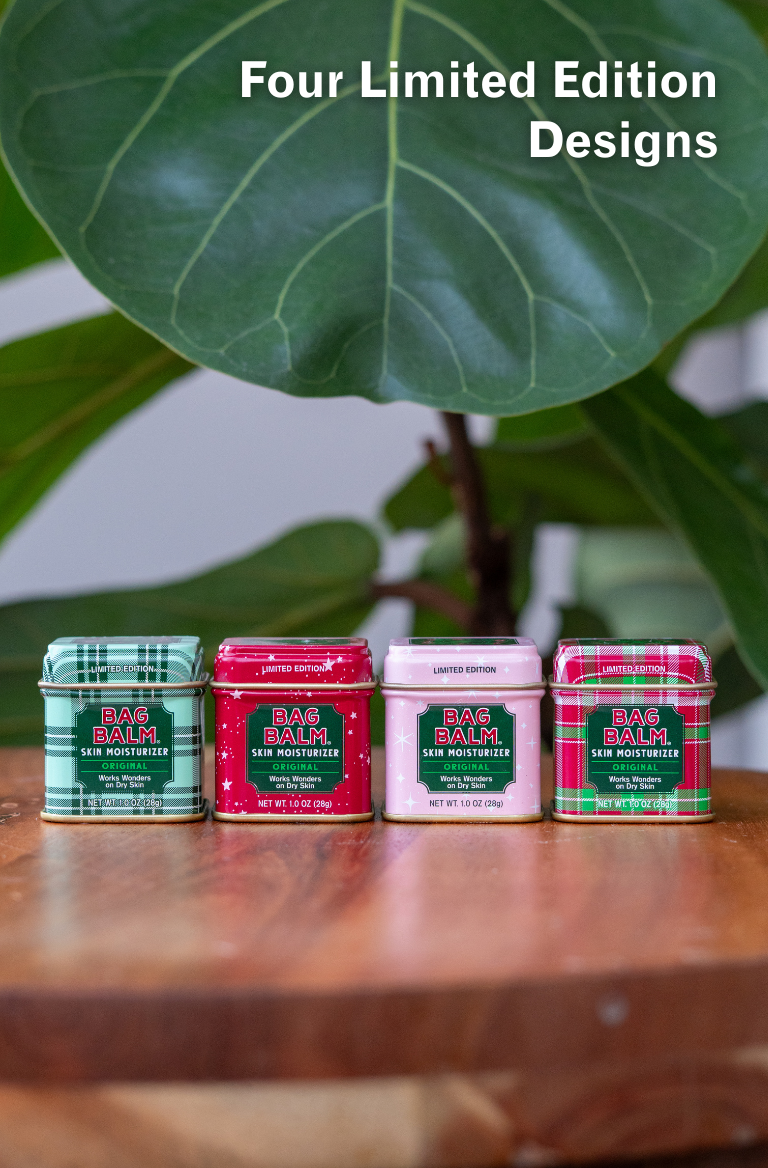 Four limited edition tins of Bag Balm on a wooden surface with green leaves in the background.